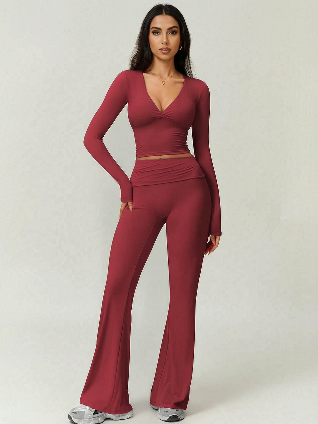 Woman wearing a burgundy long-sleeve top and flared pants on a white background