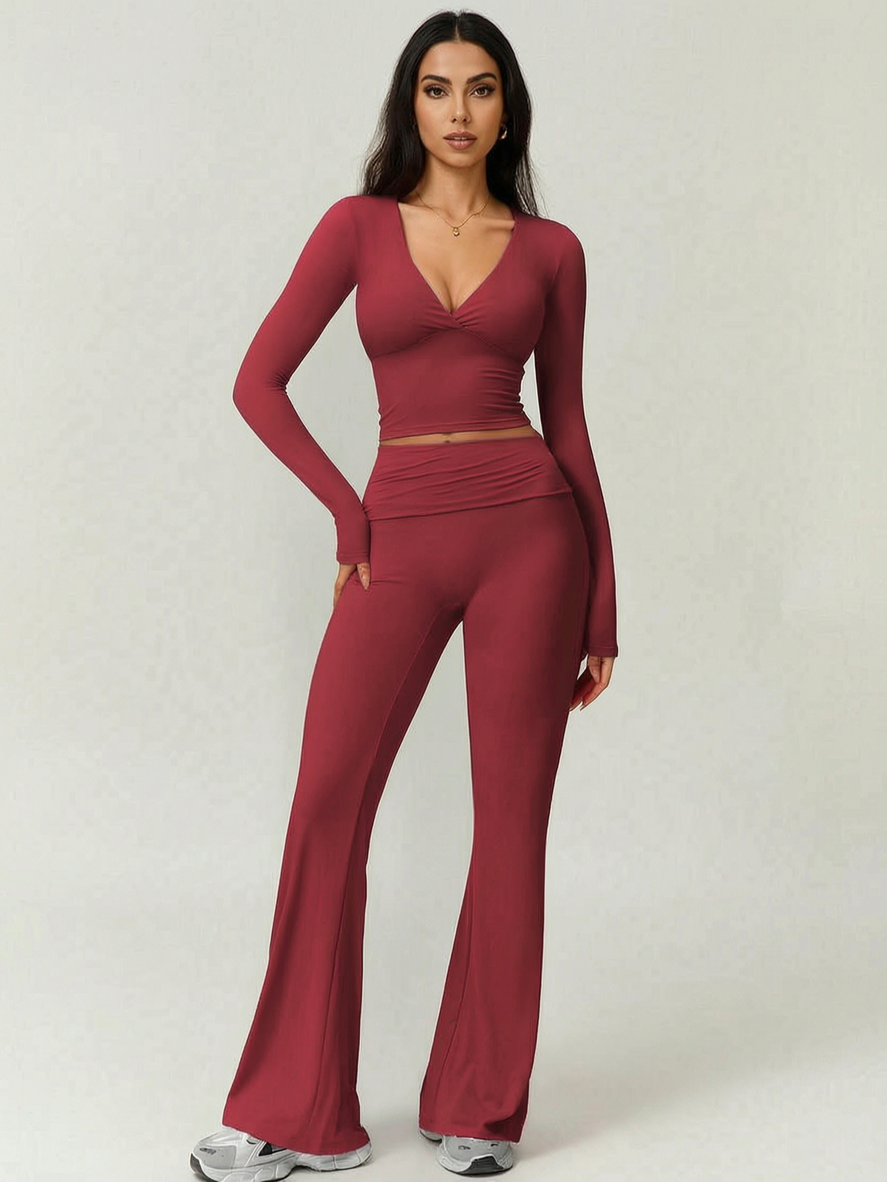 Woman wearing a burgundy long-sleeve top and flared pants on a white background